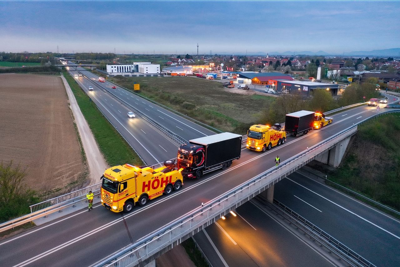 Bergefahrzeug der Höhl Gruppe schleppt einen Lkw über eine Autobahnbrücke in der Dämmerung, Luftaufnahme